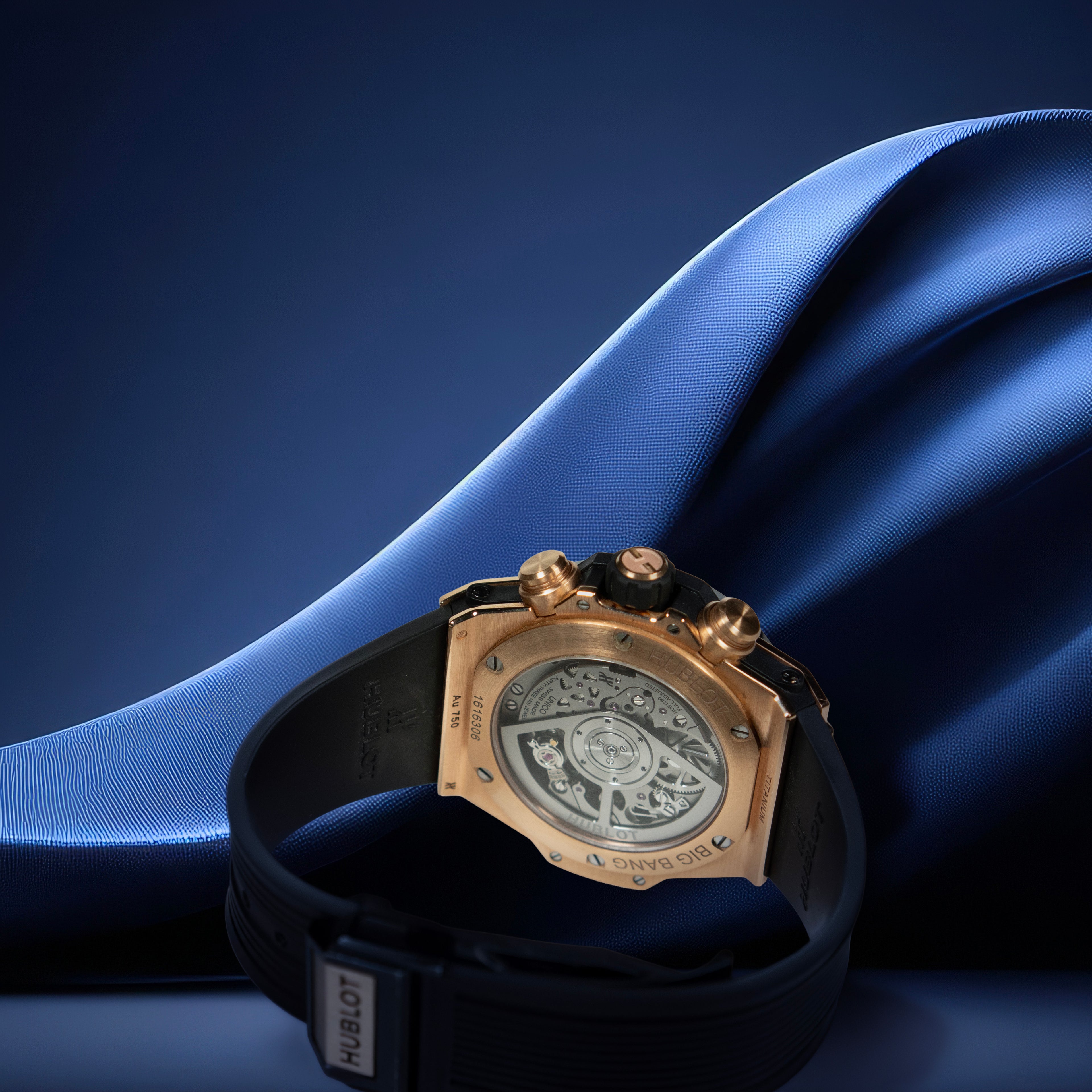 Luxury watch with black strap and gold case on blue fabric background